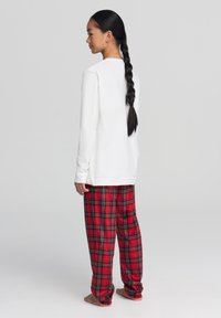 Biała bluzka z długim rękawem w zestawie z czerwonymi i czarnymi spodnimi piżamowymi w kratkę. Miękki materiał, luźny krój i wyraźny detal w kratkę.