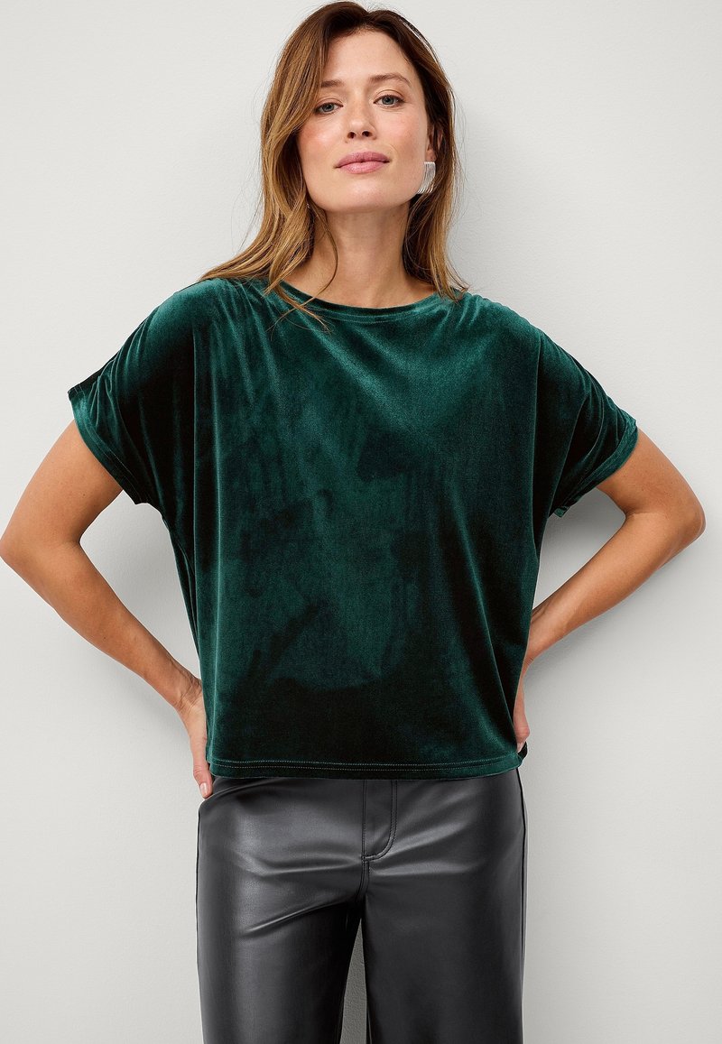 Grøn fløjlstop med en løs pasform, korte ærmer og rund halsudskæring, parret med sorte faux læderbukser. Glat tekstur og afslappet design.