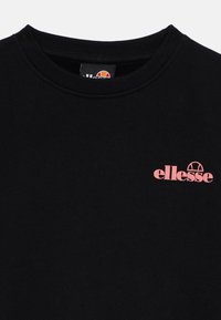 Svart sweatshirt laget av bomull, med ribbestrikket hals og en rosa "ellesse"-logo på brystet. Glatt tekstur og uformell design.