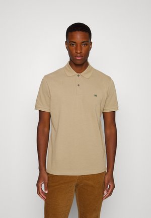 Camisa polo beige de algodón con collar clásico, mangas cortas, tapeta de tres botones y pequeño logo verde en el lado izquierdo del pecho.