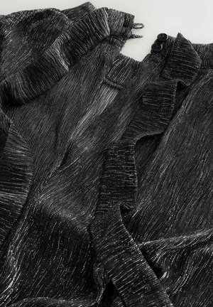 Čierna textúrovaná tkanina s kovovými striebornými vláknami; má volánové okraje a dve čierne gombíky na výstrihu.