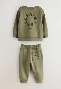 Olivgrüner Sweatshirt- und Jogginganzug. Das Sweatshirt hat einen auffälligen, kreisförmigen Text und gerippte Bündchen. Die Jogginghose hat einen elastischen Bund und eine Gesäßtasche.