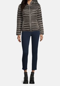 Šedá péřová bunda s vodorovným prošíváním, přední zip, odnímatelná kapuce, nošená přes tmavě modré kalhoty a černé šněrovací boty.