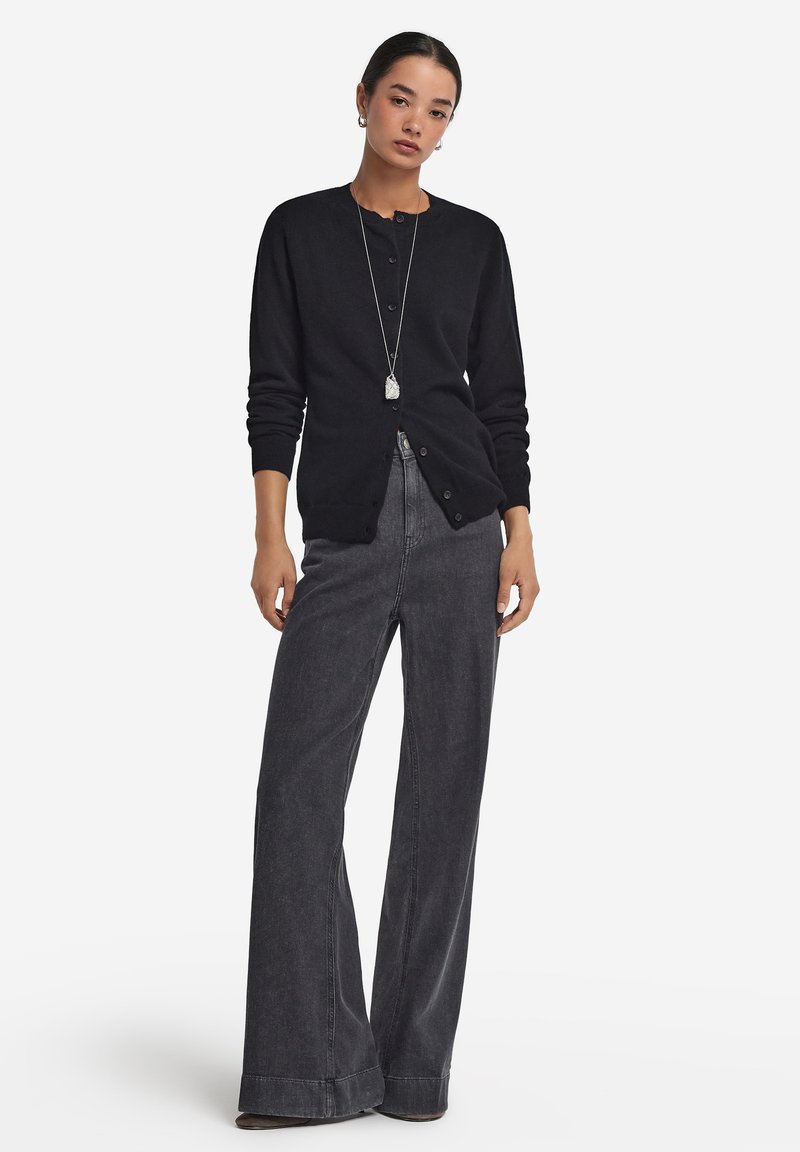 Czarny kardigan z guzikami, długimi rękawami i okrągłym dekoltem, w połączeniu z wysokim stanem szarych szerokich spodni dżinsowych. Prosta srebrna naszyjnik jako akcent.