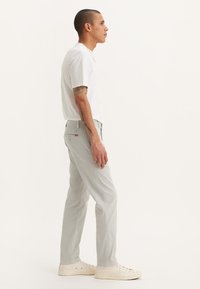 Pantalones rectos de un gris claro, confeccionados en una mezcla de algodón, combinados con una camiseta blanca de manga corta y zapatillas blancas. Diseño sencillo.
