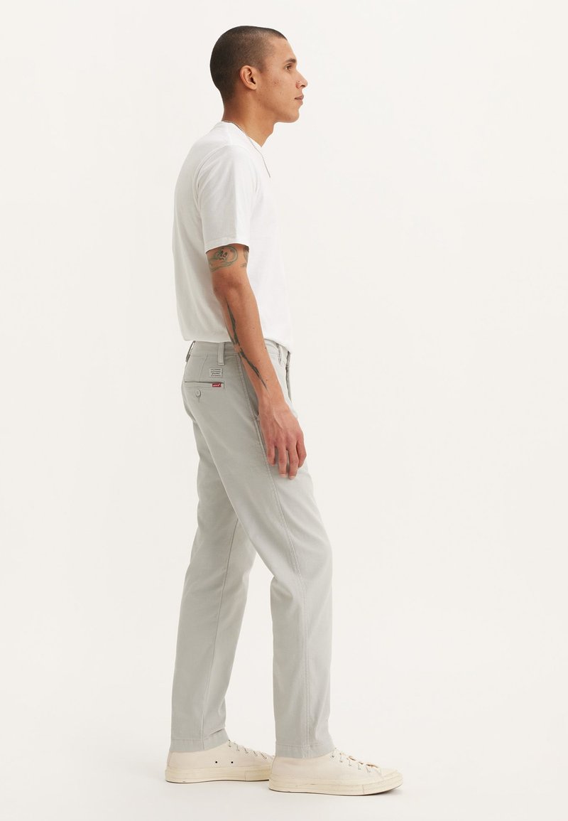 Pantalones rectos de un gris claro, confeccionados en una mezcla de algodón, combinados con una camiseta blanca de manga corta y zapatillas blancas. Diseño sencillo.