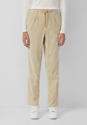Beige corduroy broek met een ontspannen pasvorm, voorzien van een elastische tailleband en een trekkoord. Gecombineerd met witte sneakers.