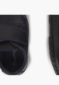 Chaussure en cuir bleu foncé avec une sangle Velcro, dotée d'un col rembourré et d'une semelle en caoutchouc noir texturé. L'intérieur est équipé d'une doublure douce.