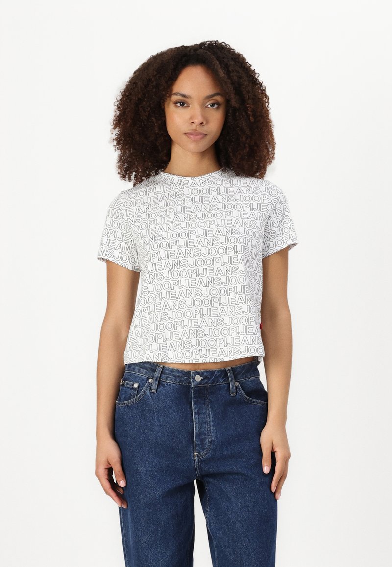 Hvit cropped T-skjorte med svart "JOOP JEANS" tekstmønster, parret med høyhalsede blå denimjeans, som har et klassisk fem-lomme-design.