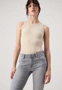 Beige ilman hihoja bodysuit pyöreällä kaula-aukolla yhdistettynä tiukkoihin vaaleanharmaisiin farkkuihin, joissa on viisi taskua ja etupainike.