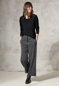 Maglietta nera a maniche lunghe abbinata a pantaloni grigi a gamba larga, con una texture sottile e tasche davanti, indossata con stivali neri alla caviglia.