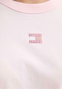 T-shirt in cotone rosa chiaro con scollo rotondo e maniche corte, con un piccolo logo "TOMMY JEANS" ricamato in un design rettangolare.