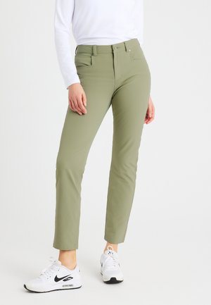 Hellgrüne, eng anliegende Hosen aus glatt verarbeitetem Material, mit vorderen Taschen und Reißverschluss. Kombiniert mit weißen Turnschuhen, was einen lässigen Look vermittelt.