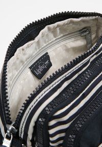 Trousse Kipling avec tissu rayé noir et blanc, fermeture éclair, poche intérieure et étiquette logo. Texture lisse et matériau durable.