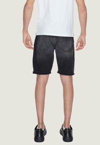 Shorts in denim nero con un design sbiadito, orli arrotolati e due tasche posteriori. Abbinati a scarpe nere, visti da dietro.