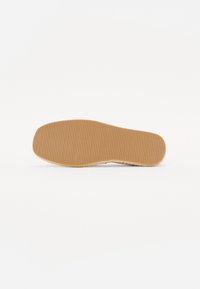 Semelle de chaussure plate en caoutchouc marron clair avec une texture à nervures verticales et une légère courbure, présentant des détails en jute le long du bord.