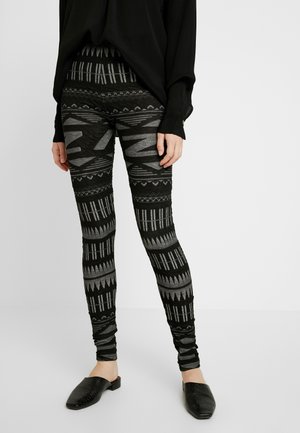 Black and gray patterned leggings with intricate geometric designs and textured fabric. Paired with black slip-on mules.