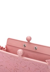 Borsa in plastica rosa con design floreale in rilievo, dotata di chiusura a scatto e due pomelli rotondi in cima per una facile apertura.