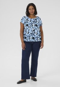 Top blu chiaro a fantasia floreale con maniche corte, abbinato a jeans svasati blu scuro e ballerine nere. Design semplice e casual.