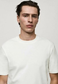 Tricou alb cu guler rotund, fabricat din bumbac moale. Mâneci scurte și o croială ușor relaxată, cu o textură netedă și detalii de design minime.