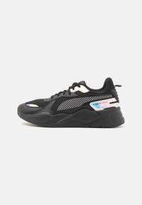 Schwarzer Sportschuh mit dicker Sohle, Obermaterial aus Mesh und Synthetik, schimmernde Akzente und gestreiftes Seitenmuster vor weißem Hintergrund.