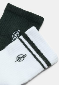 Un paio di calzini a coste, uno nero con logo bianco e uno bianco con logo nero e due strisce nere vicino al polsino.