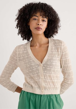 Beige gebreide cardigan met een V-hals, knoopsluiting en opengewerkte patroon. Voorzien van lange mouwen en een aansluitende zoom.