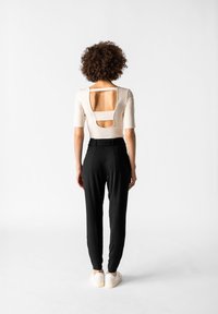 Beige figurnära topp med utskärningar på baksidan, ihop med svarta smala byxor. Modellen bär vita sneakers. Slät tyg och strukturerad design.