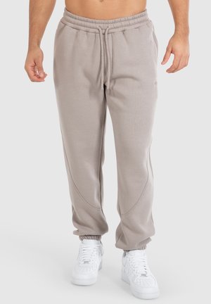 Lys grå sweatpants lavet af blødt stof med elastisk talje, snorelukning og tapered manchetter. Båret med hvide sneakers.
