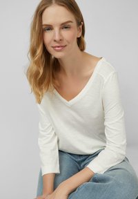 Witte, lange mouwen V-hals top gemaakt van zachte stof, vergezeld van lichtblauwe jeans. De top heeft een relaxte pasvorm en casual stijl.