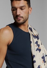 Marineblauw geribbelde tanktop, gecombineerd met een crèmekleurige sjaal met blauwe bloemenpatronen. De gladde textuur en de getailleerde pasvorm benadrukken het ontwerp.