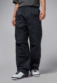 Schwarze Cargo-Hosen mit einem elastischen Bund, Seitentaschen und einer lockeren Passform. Der Stoff ist strukturiert und leicht und wird mit weißen Turnschuhen kombiniert.