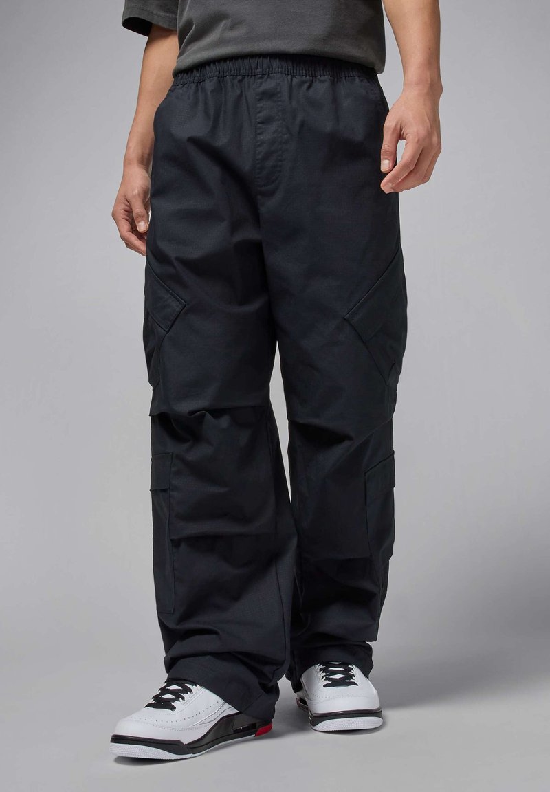 Schwarze Cargo-Hosen mit einem elastischen Bund, Seitentaschen und einer lockeren Passform. Der Stoff ist strukturiert und leicht und wird mit weißen Turnschuhen kombiniert.