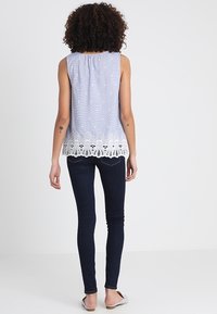 Top sin mangas de color azul claro con rayas blancas y un dobladillo de encaje. Combinado con jeans ajustados oscuros y zapatos planos. Diseño de tela simple y texturizada.