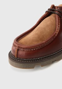 Zapato de cuero y ante marrón con punta redondeada, detalles cosidos y suela de goma texturizada para mayor tracción. Acabado liso en las secciones de cuero.
