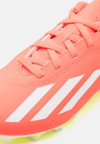 Scarpe da calcio sintetiche arancioni con strisce bianche, caratterizzate da una tomaia testurizzata e lacci in contrasto, progettate per la presa e l'agilità.