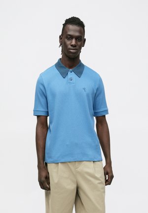 Κοντομάνικο πόλο μπλουζάκι σε ανοιχτό μπλε χρώμα, με γιακά σε πιο σκούρο μπλε, κουμπιά μπροστά και διακριτική υφή. Κανονική εφαρμογή και απλό κεντητό λογότυπο.