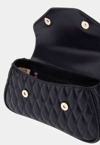 Borsa in pelle nera trapuntata con chiusure a pulsante dorate, flap aperto che rivela una tasca interna con zip e foderatura beige.