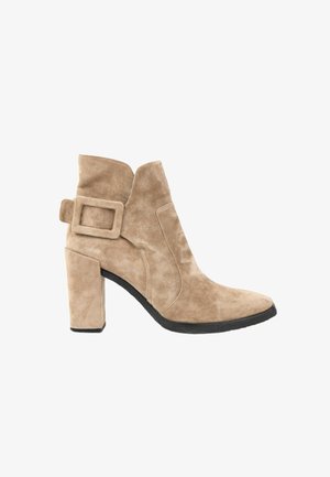 Bottine beige en daim avec un talon haut et épais, un bout pointu et une grande boucle carrée sur le côté.