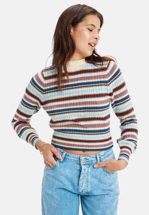 Gestreepte gebreide trui met ribbeltextuur in blauw, bruin, roomkleur en perzikachtige tinten, gecombineerd met hoge, lichtblauwe jeans.