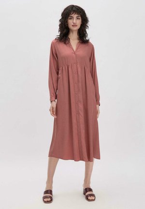 Rosenfarbenes Langarmkleid mit knöpfbarem Vorderteil, tailliertem Oberteil und ausgestellt Rock. Glattes Material und spitzer Kragen. Braune Sandalen.