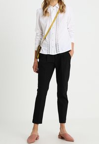 Witte knoopshirt met verticale versieringen, zwarte tapered broek en lichtroze instappers. Gele schoudertas.