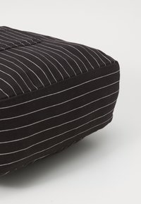 Cojín de tela negra con rayas blancas, forma rectangular y detalles de costura visibles. La textura parece suave y lisa.