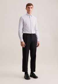 Camicia bianca con piccolo motivo geometrico nero, abbinata a pantaloni neri a vita alta. Scarpe nere stringate completano l'outfit.