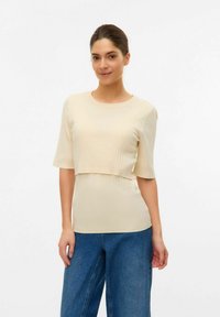 Top a costine beige con maniche corte e design cropped. Texture liscia, scollatura rotonda, abbinato a pantaloni di denim larghi.