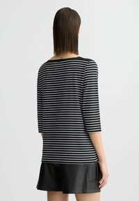 Zwart-wit gestreepte top met driekwart mouwen, ronde halslijn en een klein knoopdetail op de rug. Soepele katoenmateriaal.