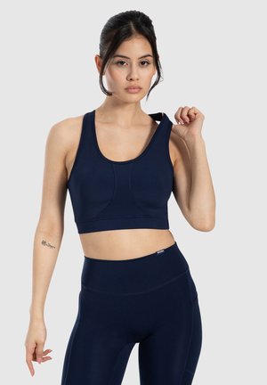 Sujetador deportivo azul marino con tirantes anchos y escote redondeado. Tela lisa y elástica con detalles de costura. Combinado con leggings de talle alto a juego.