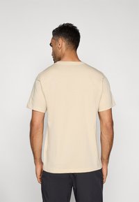 Μπεζ κοντομάνικη μπλούζα με στρογγυλή λαιμόκοψη, κατασκευασμένη από βαμβάκι, με ομαλή υφή. Προβολή από πίσω, που δείχνει μια άνετη εφαρμογή.