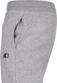Grijze sweatpants van zacht materiaal met een elastische band, voorzien van een zijzak en een klein zwart logo-accent op de linker bovenbeen.