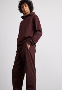 Burgundijas krāsas hoody ar priekšējo kangaroo kabatu, ar augstu apkakli un ribotām piedurknēm, apvienots ar atbilstošām biksēm ar sānu kabatām.